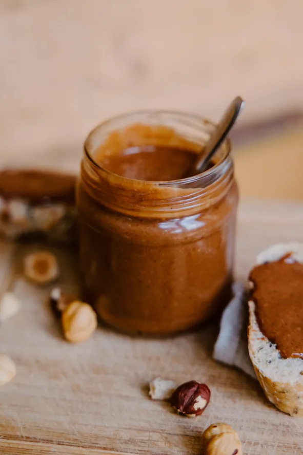 Pot en verre de pâte à tartiner avec une cuillère, à côté d'une tartine